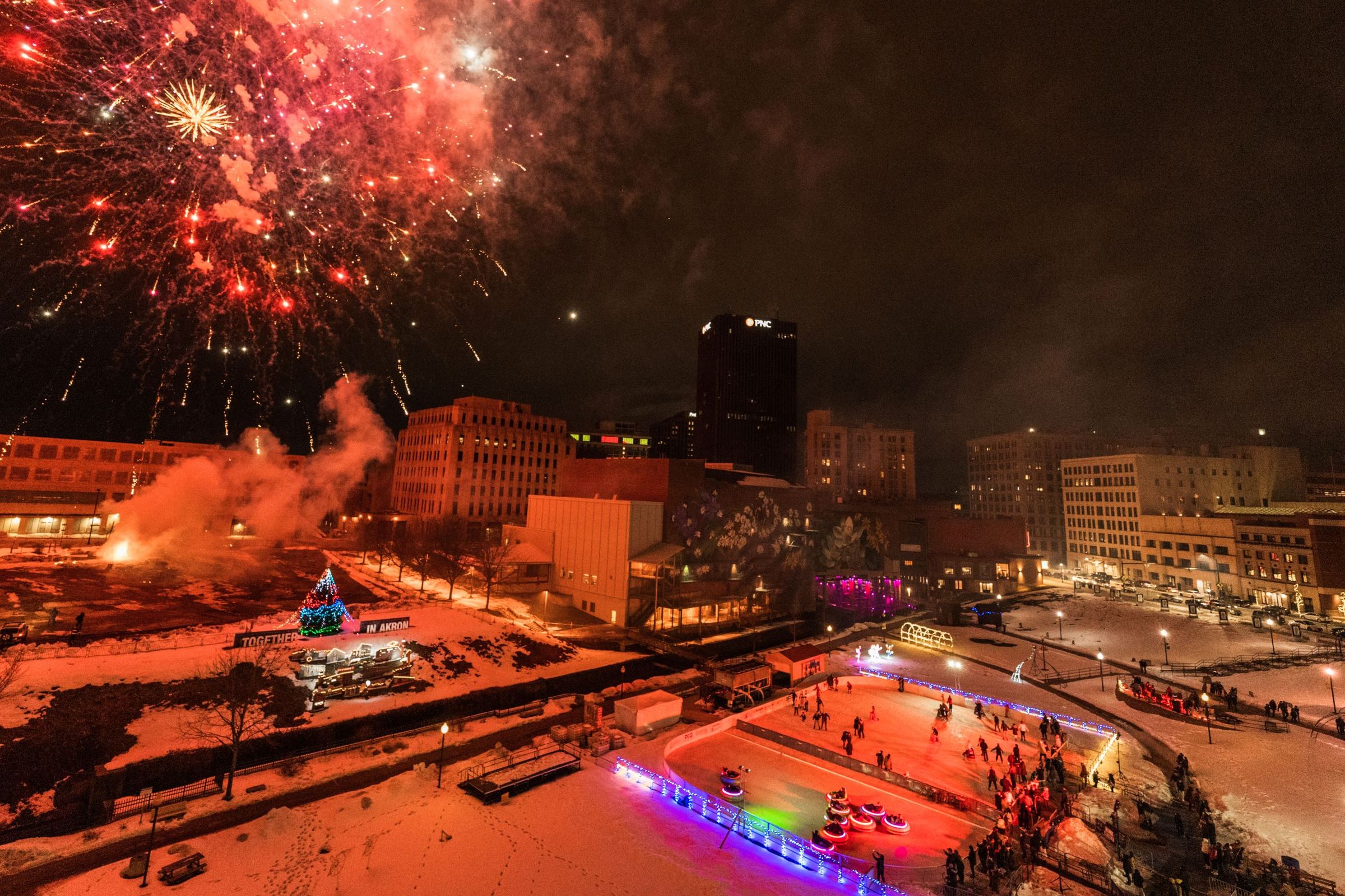 Red and gold fireworks over Lock 3 Park in Akron, Ohio, with clusters of people standing on the ground