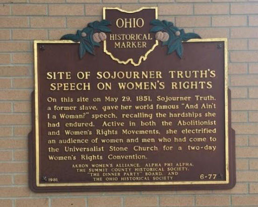 A brown and gold historical marker hanging on an exterior brick wall